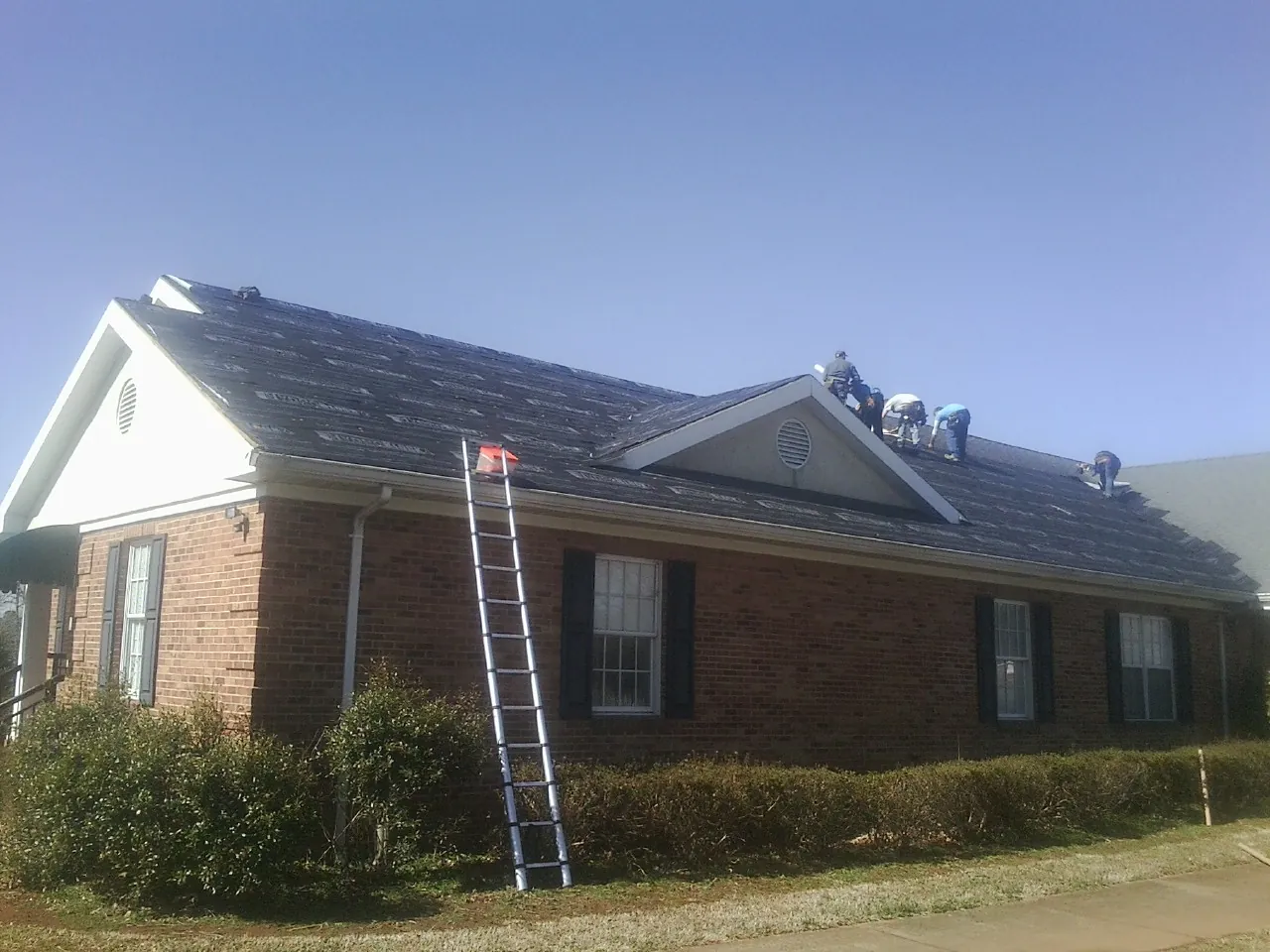 Crew tearing shingles off a brick ranch roof with a ladder set — Emergency Roof Repair work by our crew in Newton Upper Falls
