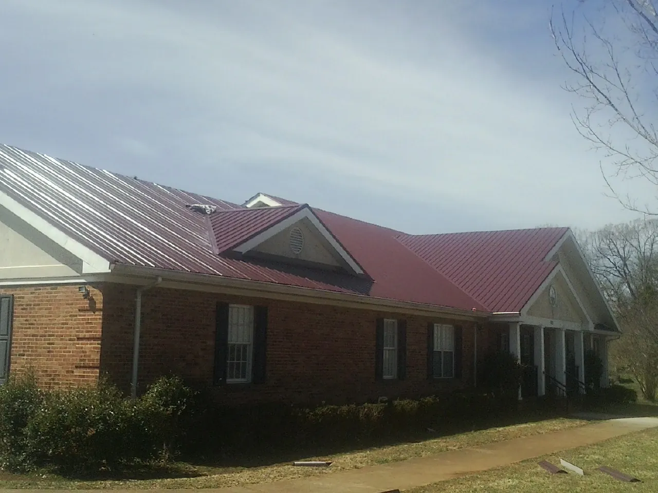 Red metal roof with gabled entries on a long brick building, from a Hail Damage Roof Repair job in Newton Upper Falls