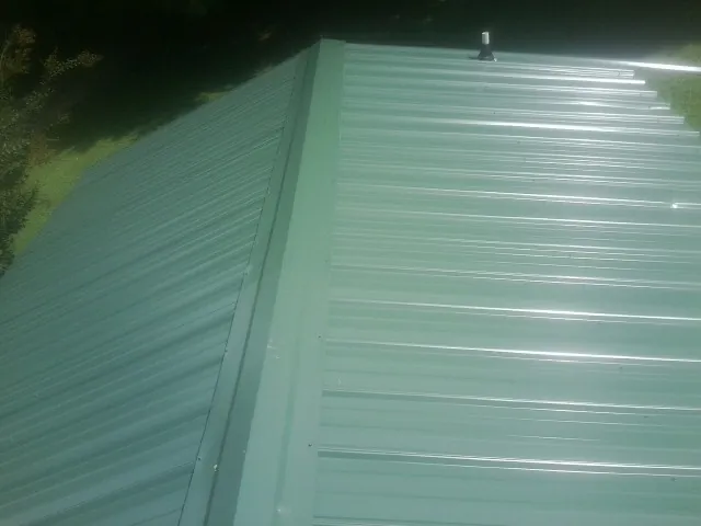 New green metal panels meeting at the ridge of a roof — Flat Roof Repair work by our crew in Newton Upper Falls