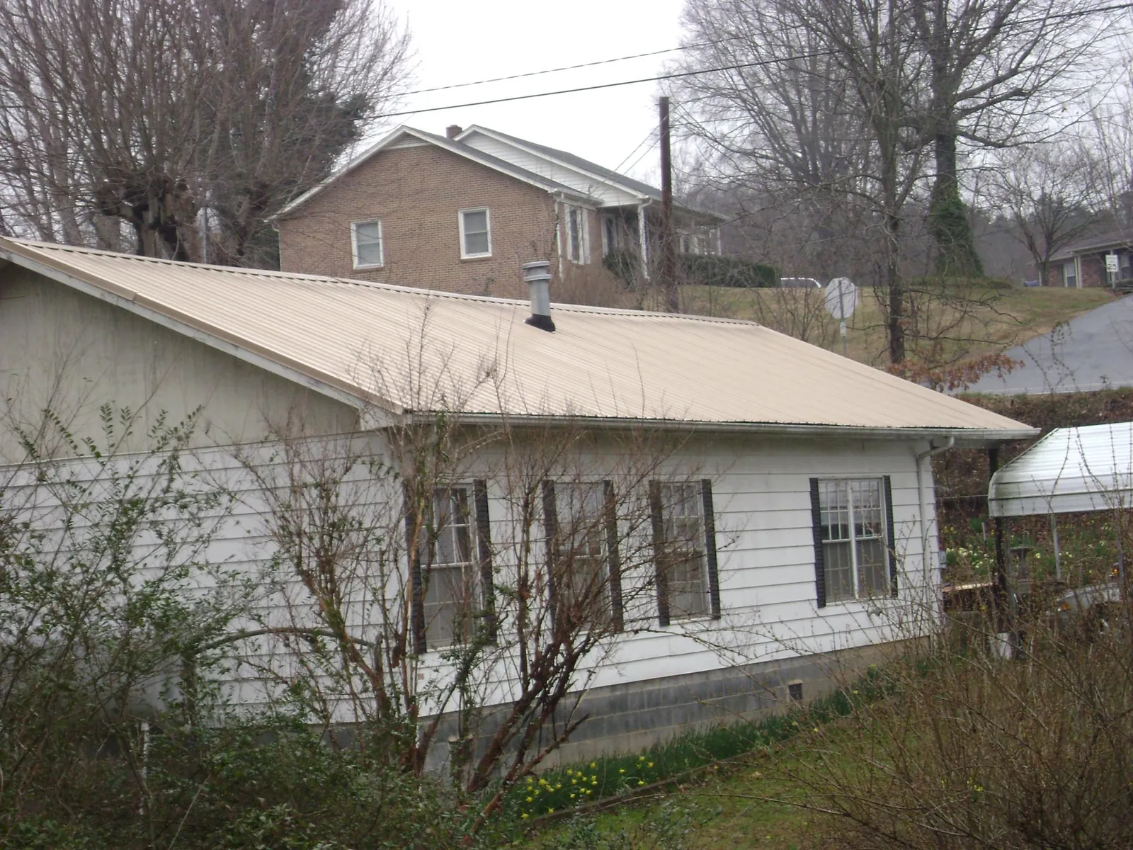 Tan metal roof on a white sided house set into a hillside — Commercial Roofing by Roofing Brothers in Newton Upper Falls