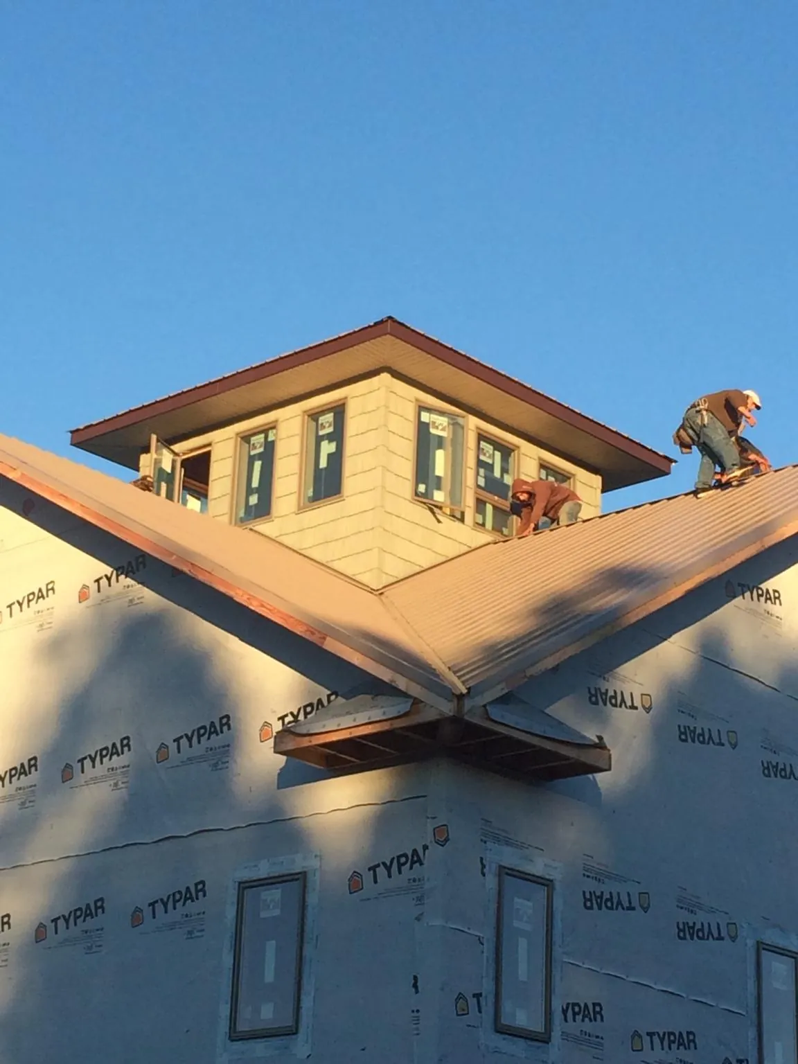 Roofers working around a rooftop cupola on a new metal roof at sunset — Roof Waterproofing in Newton Upper Falls by Roofing Brothers